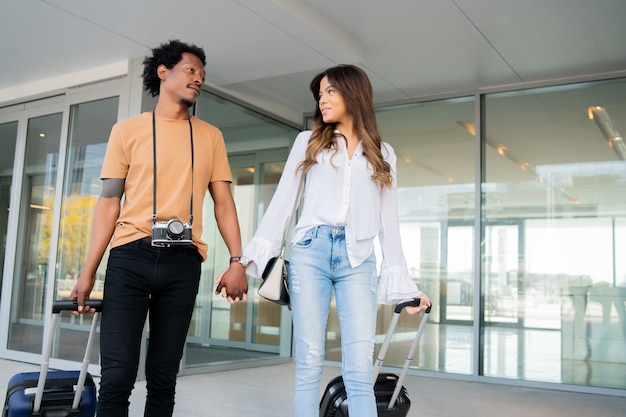 Portrait of young tourist couple carrying suitcase while walking outdoors on the street. Tourism concept.