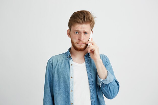 Portrait of young upset man talking on phone looking at camera.