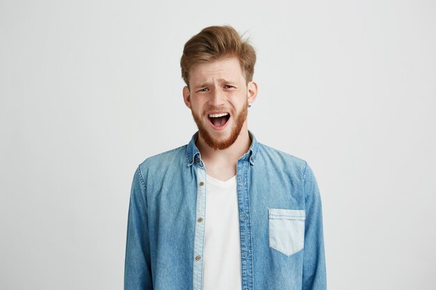 Portrait of young upset man with opened mouth frowning looking at camera.