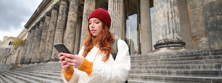Free Photo portrait of young urban girl with backpack using smartphone walking around city looking at map on