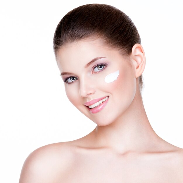 Portrait of young woman applying cream on her pretty face - white background.