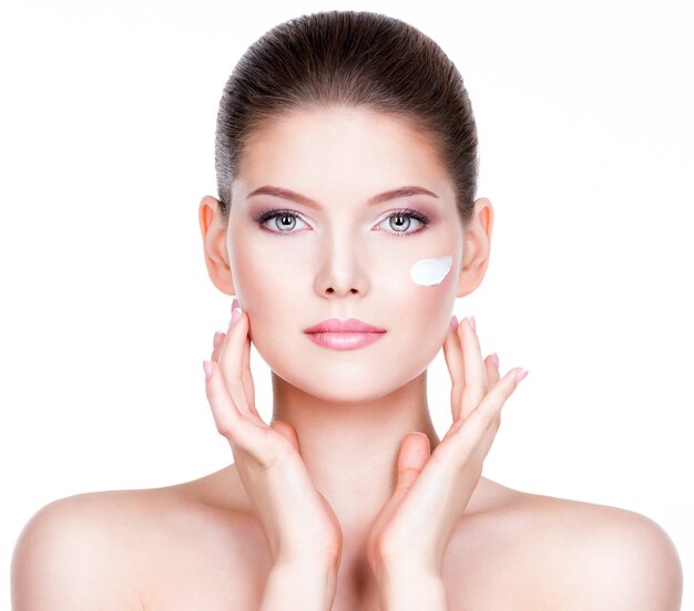 Portrait of young woman applying cream on her pretty face - over white wall.