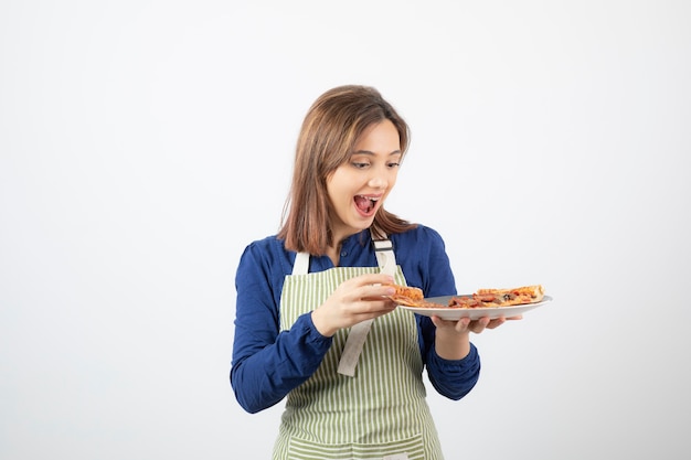 흰색으로 맛있는 피자를 보고 있는 앞치마를 입은 젊은 여성의 초상화