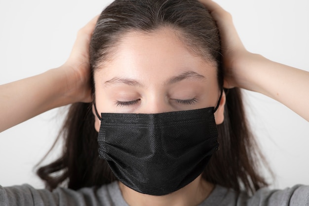 Portrait of young woman in black face mask holding her head. 