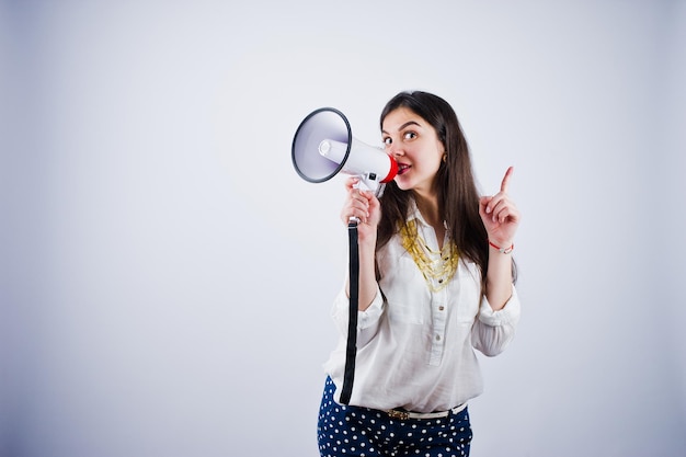 Portrait of a young woman in blue trousers and white blouse posing with megaphone in the studio