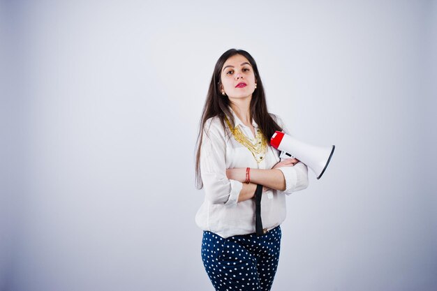 Portrait of a young woman in blue trousers and white blouse posing with megaphone in the studio