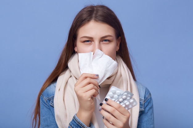 Portrait of young woman catching cold and holding pills in hands