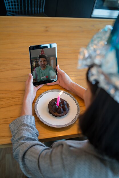 집에서 디지털 태블릿과 케이크로 화상 통화를 하며 생일을 축하하는 젊은 여성의 초상화