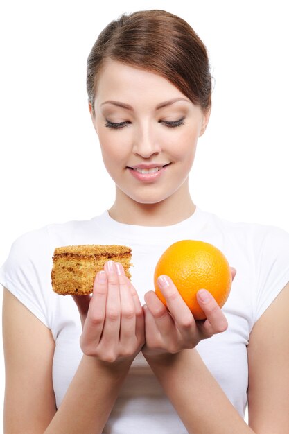 Portrait of young woman choosing between cake and orange