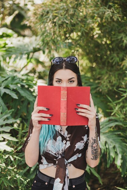 Portrait of a young woman covering her mouth with red book