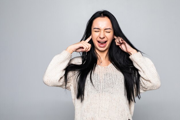 Portrait of young woman covering with hands her ears, isolated over white wall