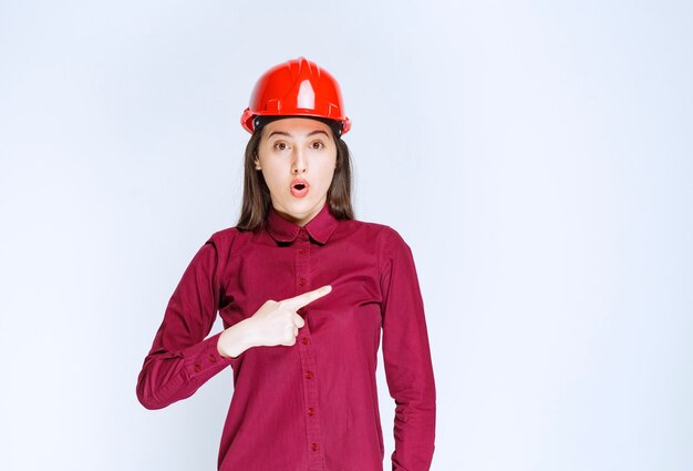 Portrait of young woman in crash helmet pointing aside . 