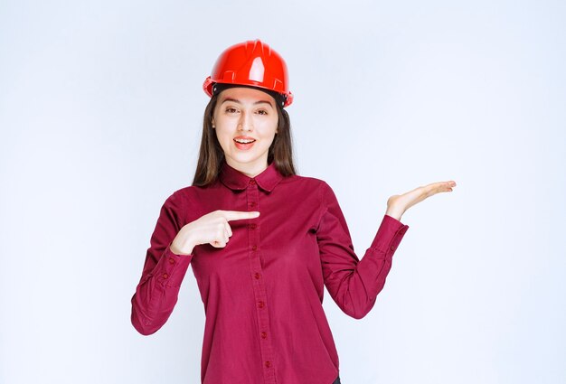 Portrait of young woman in crash helmet pointing at opened palm . 