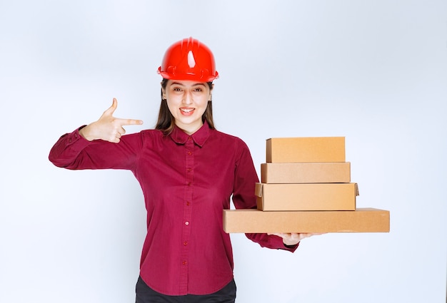 Portrait of a young woman in crash helmet pointing at paper boxes . 