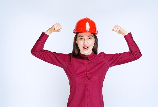 Portrait of young woman in crash helmet showing her muscle . 