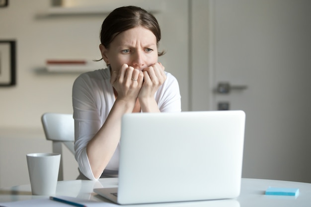 Portrait of a young woman at desk with laptop, fear