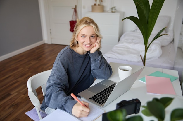 Free photo portrait of young woman distance learning working from home with laptop making notes student