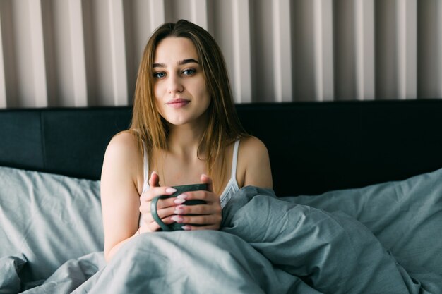 自宅のベッドでコーヒーを飲む若い女性の肖像画