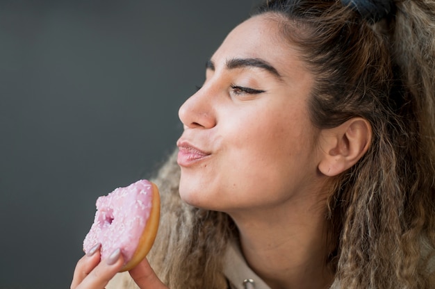 Free photo portrait of young woman eating a doughnut