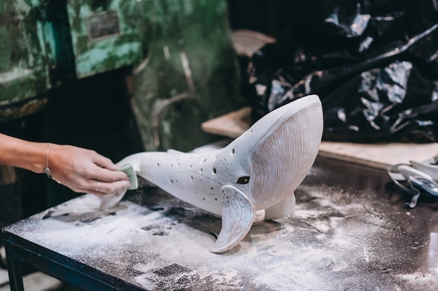 Portrait of young woman enjoying favorite job in workshop. The potter carefully works on the ceramic whale