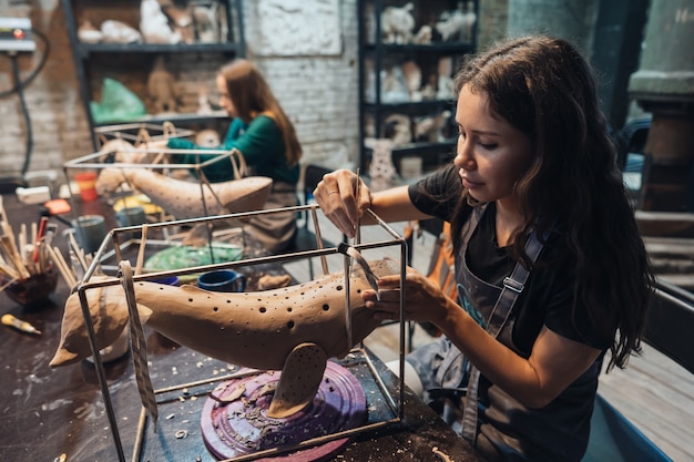 Portrait of young woman enjoying favorite job in workshop. potter carefully works on the clay whale