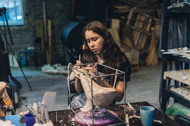 ワークショップで好きな仕事を楽しんでいる若い女性の肖像画。陶芸家は粘土クジラに注意深く取り組んでいます