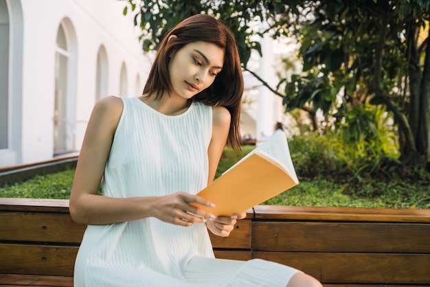 自由な時間を楽しんで、屋外に座って本を読んでいる若い女性の肖像画。ライフスタイルのコンセプト。