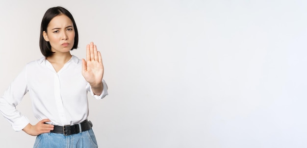 Portrait of young woman extending one hand stop taboo sign rejecting declining something standing over white background