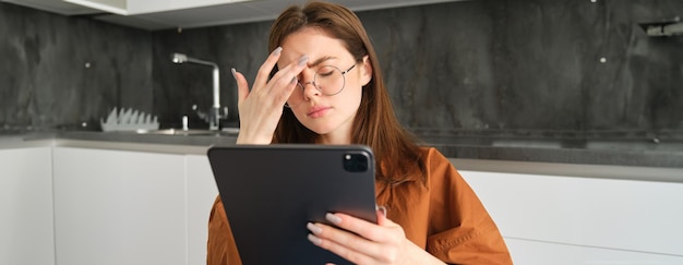 Portrait of young woman feeling unwell touching head has headache or migraine reading on digital