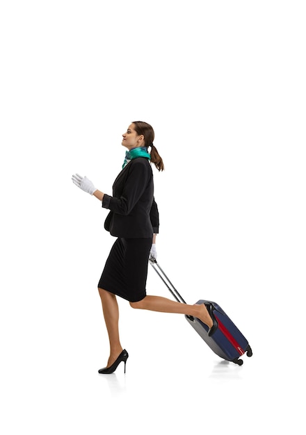 Portrait of young woman, flight attendant running with suitcase isolated on white background