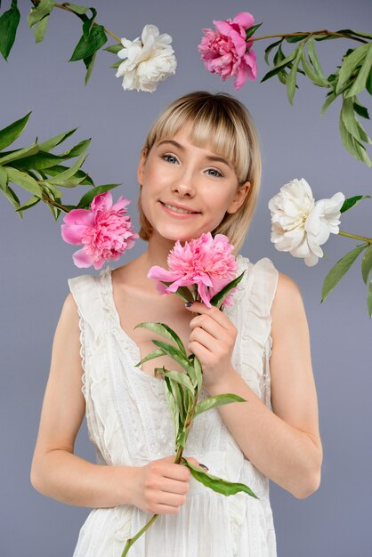 Portrait of young woman among flowers over grey wall