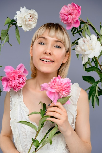 Portrait of young woman among flowers over grey wall