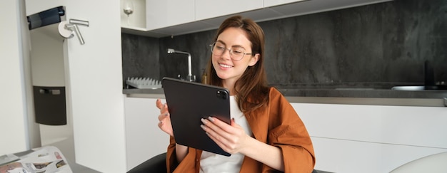 집에서 일하는 디지털 태블릿을 보는 안경을 입은 젊은 여성의 초상화가 원격으로 연결됩니다.