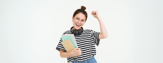 Foto gratuita ritratto di giovane donna in occhiali che indossa le cuffie sopra il collo che tiene i quaderni del pianificatore e studia