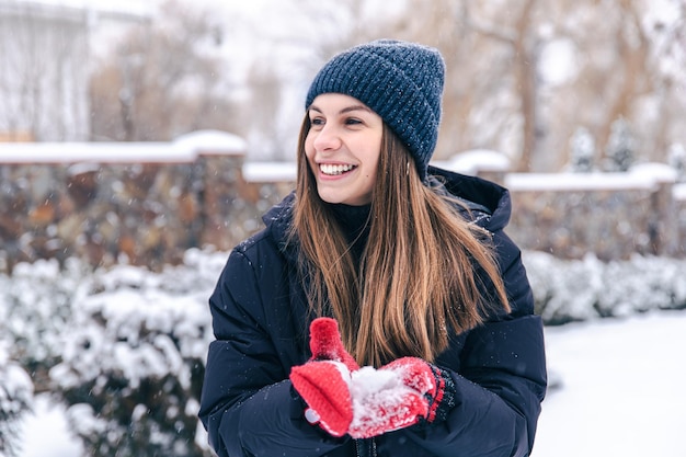 Portrait of a young woman in a hat and red mittens in snowy weather