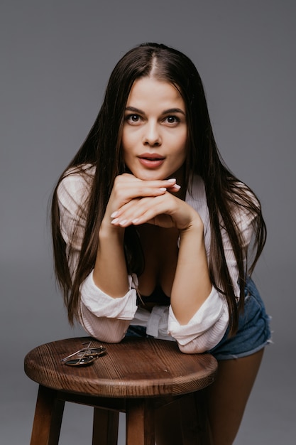 Portrait of a young woman in hat sitting on chair isolated on the gray