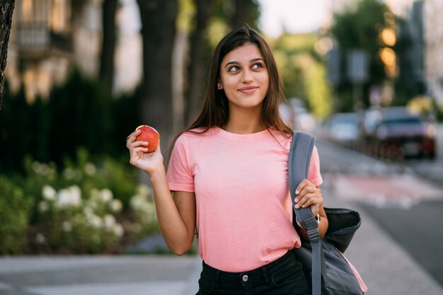 Portrait of a young woman holding apple against a street background