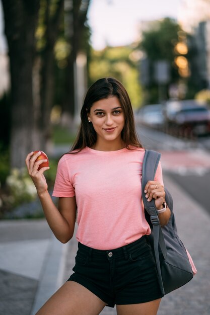 Portrait of a young woman holding apple against a street background