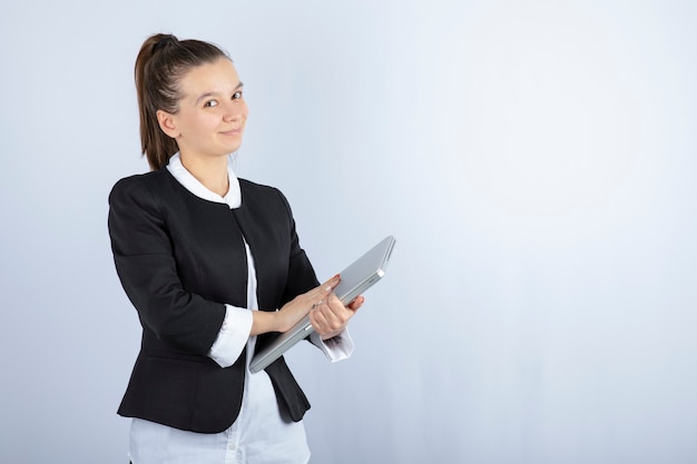 Portrait of young woman holding laptop over white wall.
