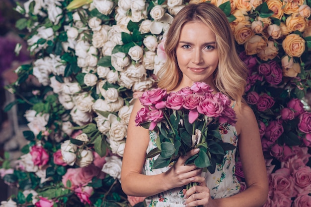 花の背景に対してピンクのバラの花束を保持している若い女性の肖像画