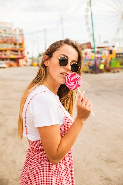 Free photo portrait of young woman holding red lollipop at amusement park