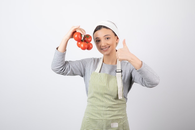 Free photo portrait of young woman holding red tomatoes over white wall