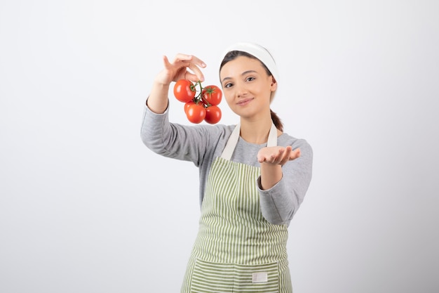 Portrait of young woman holding red tomatoes over white wall