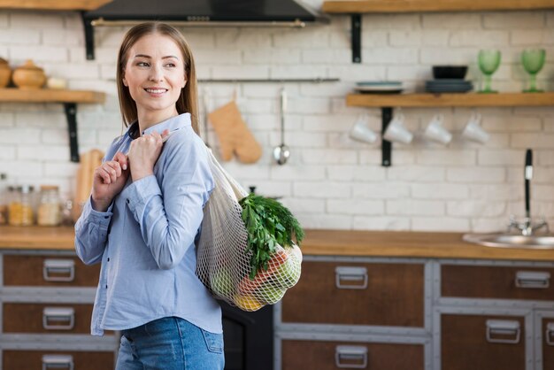 Portrait of young woman holding reusable bag with groceries