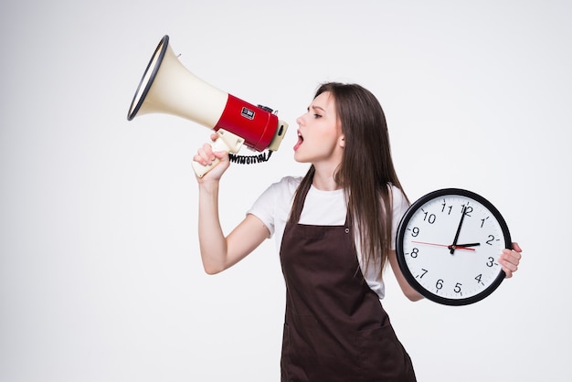 Free photo portrait of young woman holding round clock, scream in megaphone isolated.