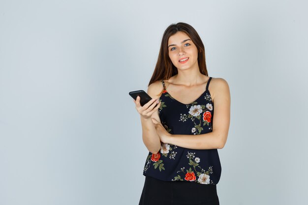 ブラウス、スカート、陽気な正面図でスマートフォンを保持している若い女性の肖像画