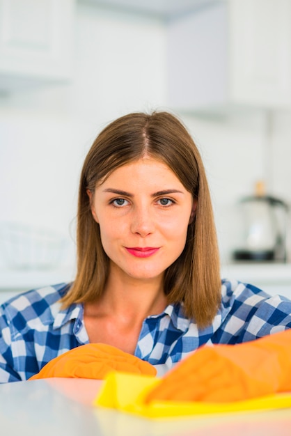 Portrait of a young woman holding yellow duster on white surface