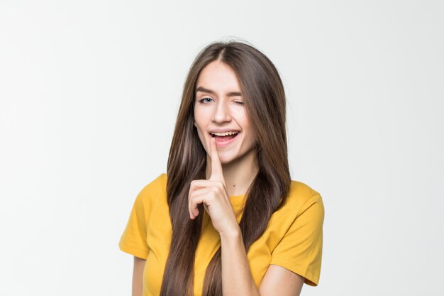 Portrait of young woman keeping finger on her lips and asking to keep quiet isolated over white wall