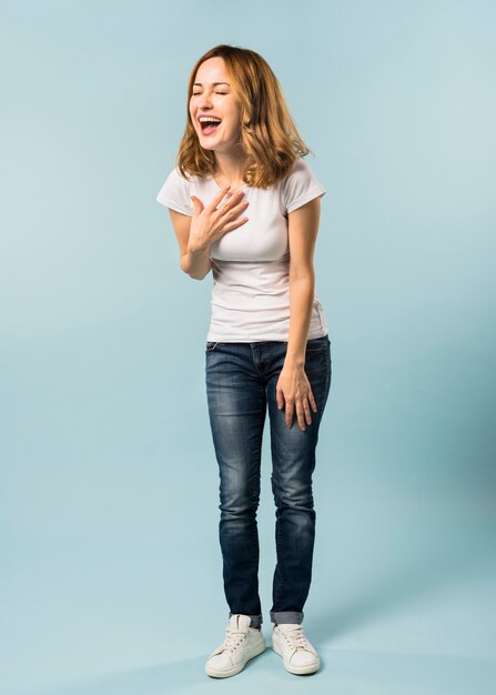 Portrait of a young woman laughing against blue background