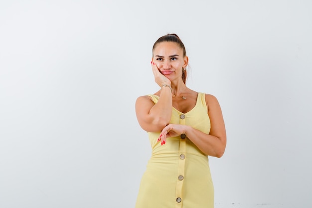 Ritratto di giovane donna che si appoggia sulla guancia sul palmo, guardando lontano in abito giallo